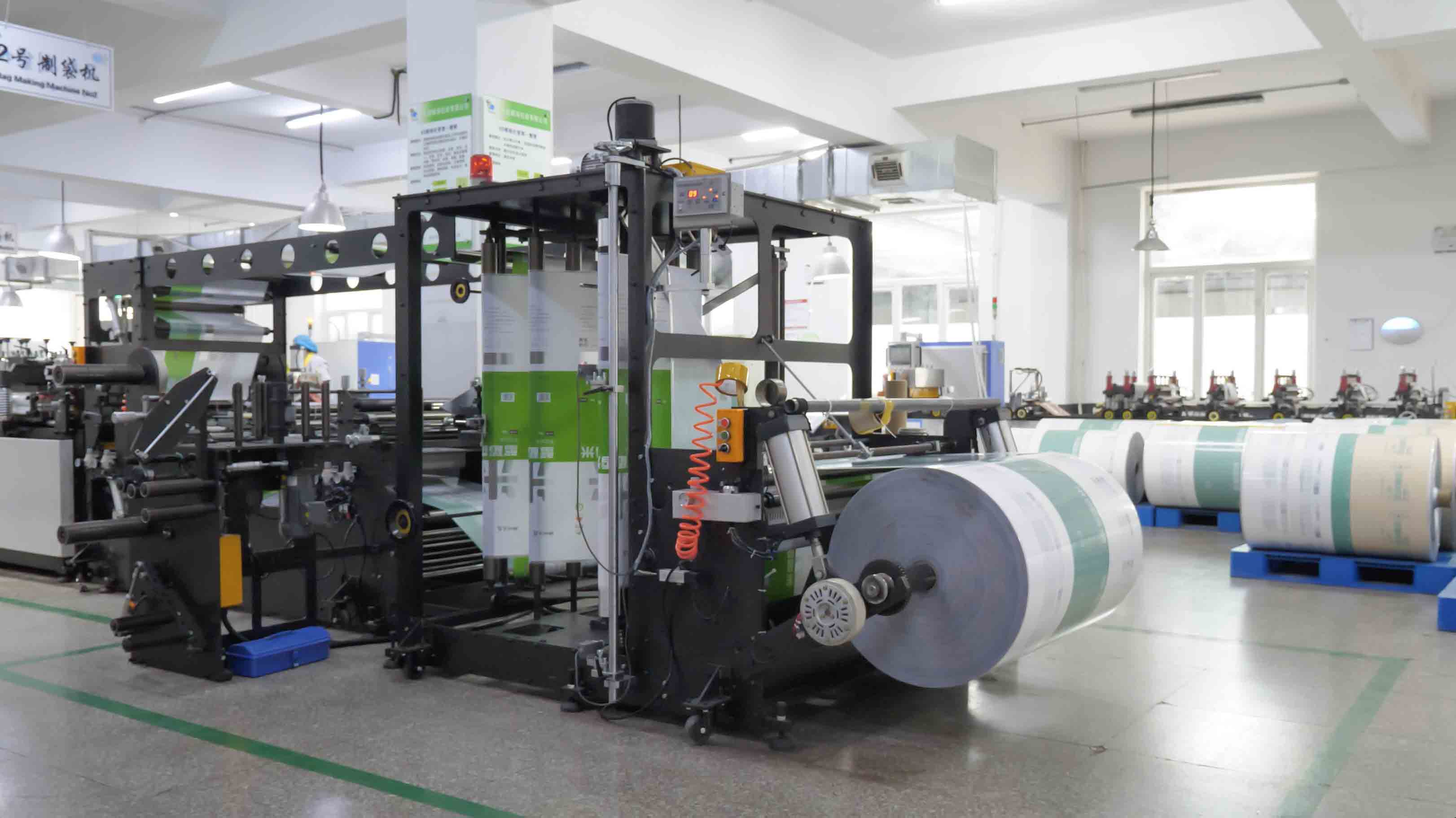 Film rolls and converting machinery visible in a flexible-packaging factory.