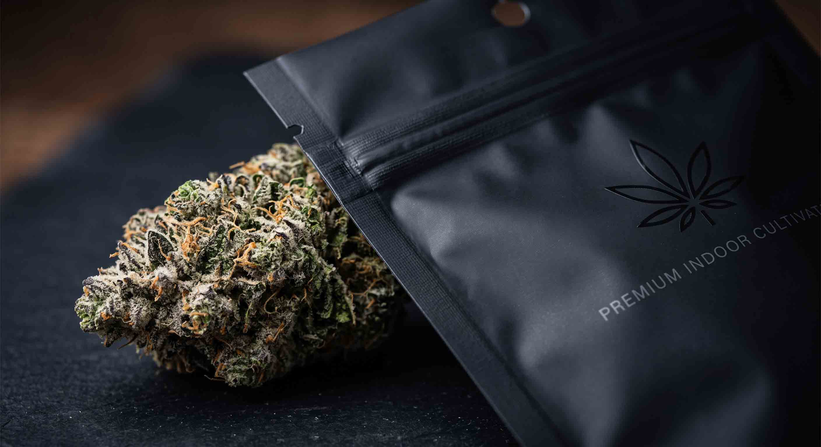 Premium indoor cannabis flower next to matte black mylar packaging bag