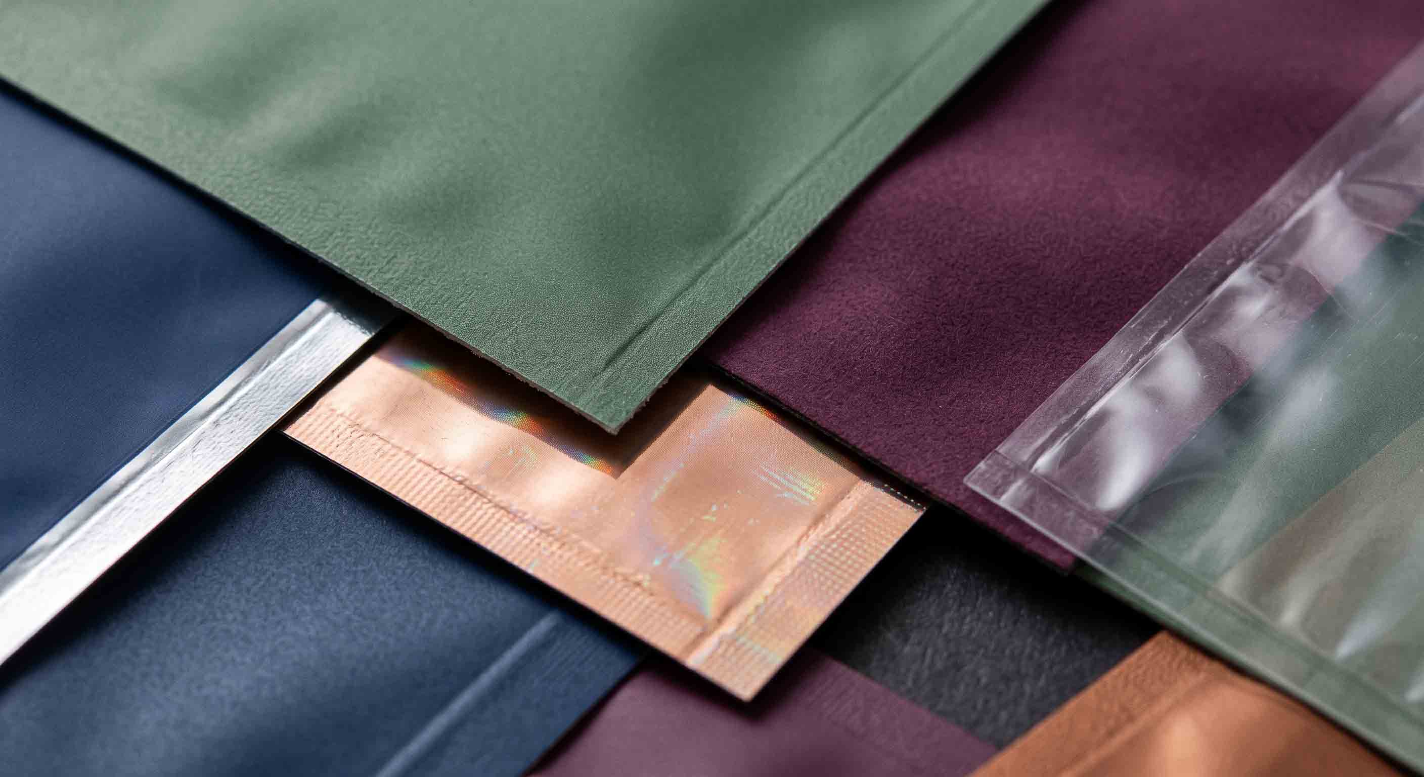 Macro view of flexible-pouch material samples with matte, metallic, clear, and reflective surface details.